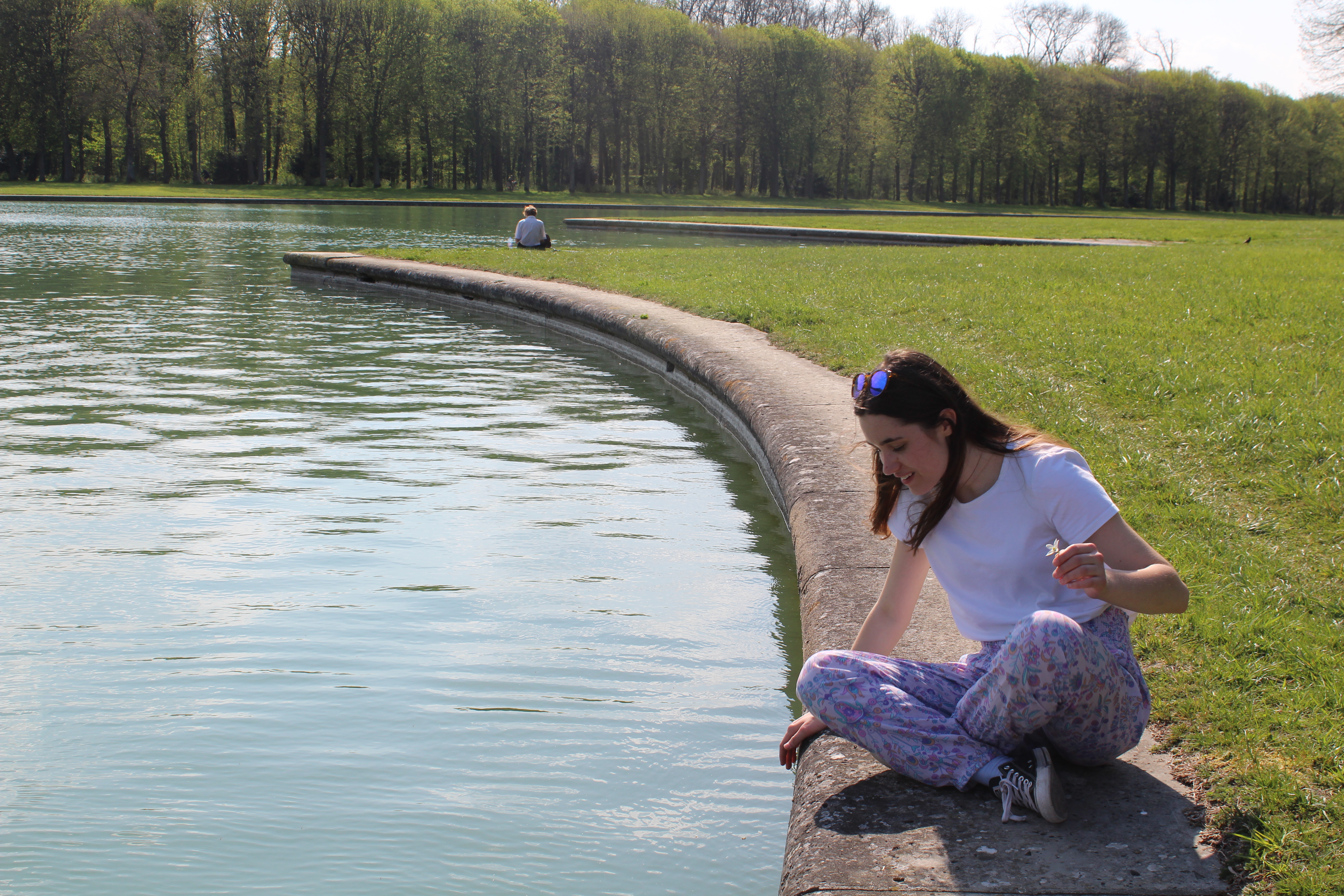 Jenny J gazing into the water of a pond in Versailles.